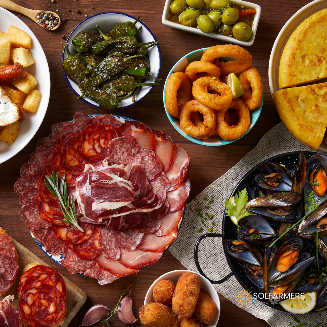  Table full of Spanish food dishes, with a variety of tapas, such as preserves, Spanish omelette, croquettes, Iberian ham, and sausages.