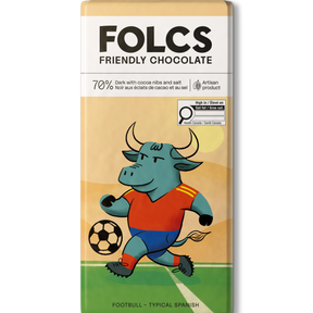 A bar of FOLCS Friendly Chocolate featuring a colorful illustration of a bull soccer player on a field. The packaging is cream and beige with a white top section containing the brand name 'FOLCS' and product details.